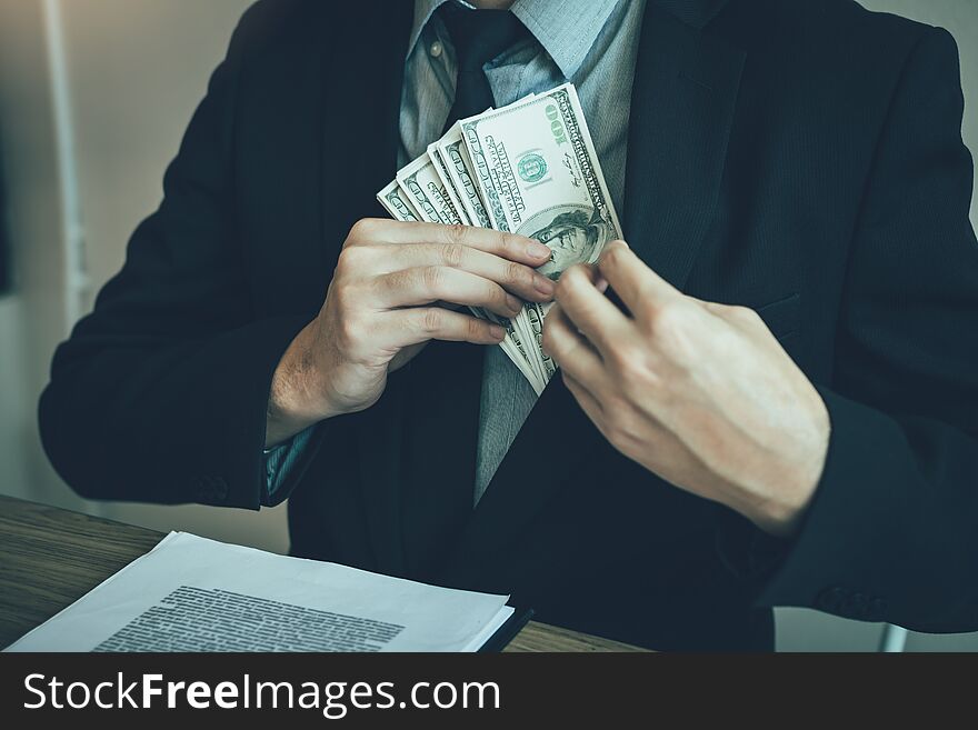 Businessman putting stack of money bills in his suit coat pocket
