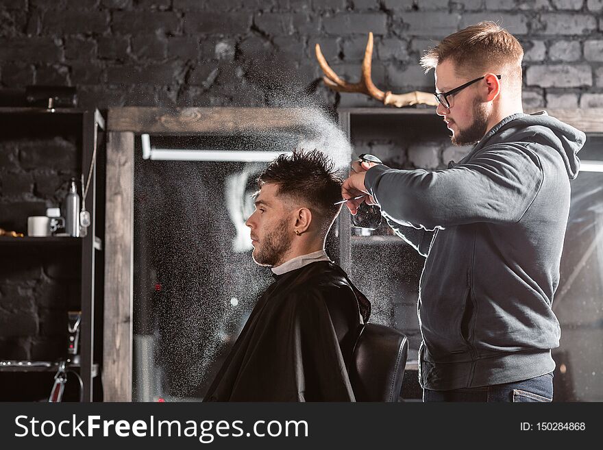 Barber sprays clean water on head in barbershop. Professional trimmer tool cuts beard and hair on young guy in barber