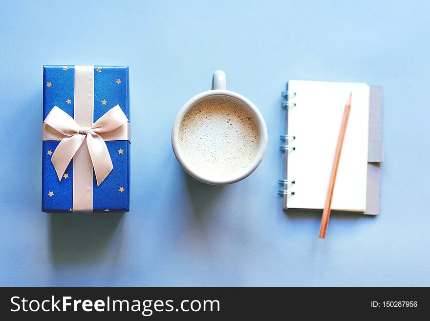 Simple layout, top view of a gift box, a mug of coffee and a notebook, conceptual set on a blue background