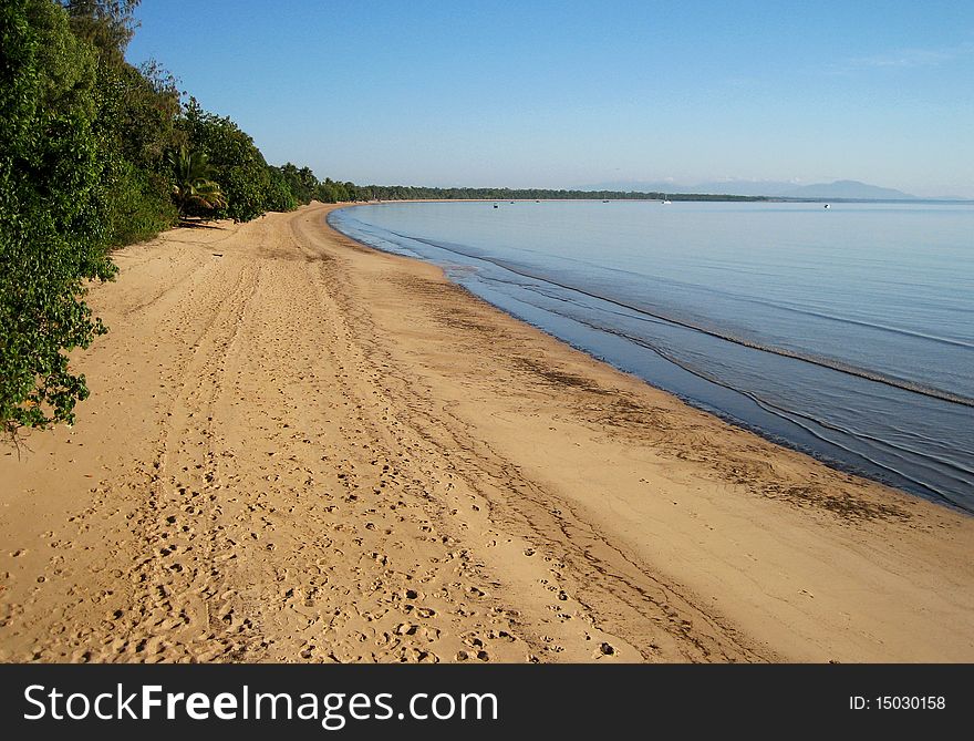 Calm waters against a blue sky and tree lined sandy beach with lots of footprints. Calm waters against a blue sky and tree lined sandy beach with lots of footprints.