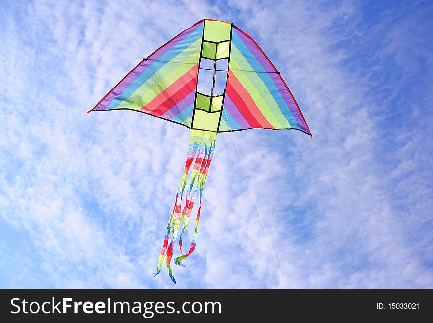 Bright multicolored kite in blue cloudy sky. Bright multicolored kite in blue cloudy sky