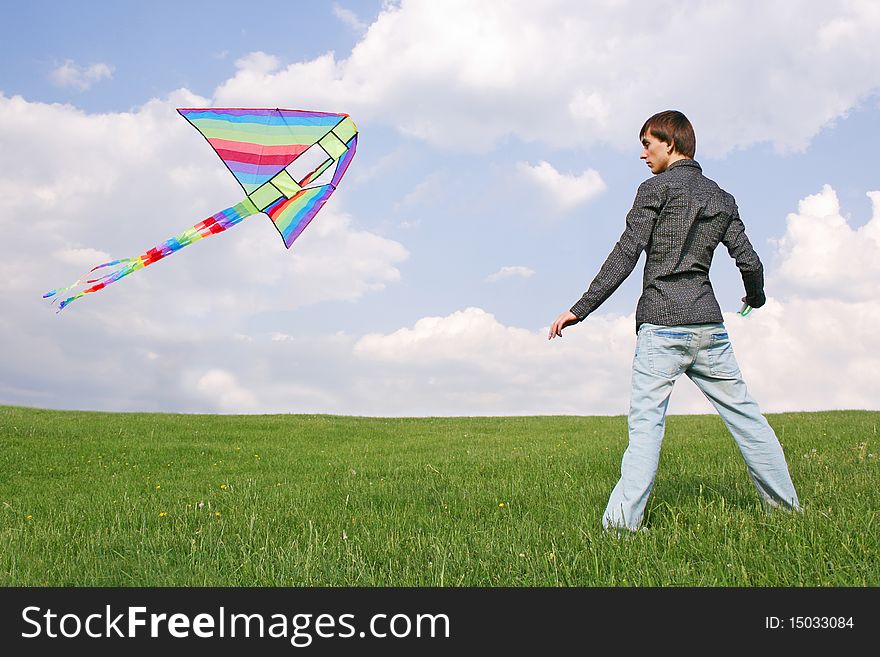 Young man in black shirt flying multicolored kite at summer time