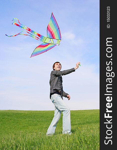 Young man in black shirt flying multicolored kite at summer time