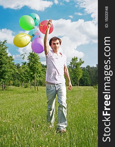 Young man with many colored balloons at green summer lawn
