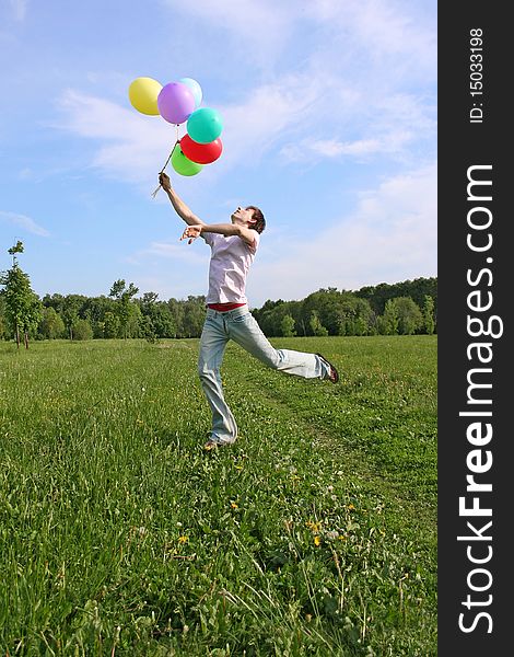 Young man with many colored balloons jumping at green summer lawn