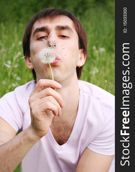 Young man blowing at dandelion focus on flower