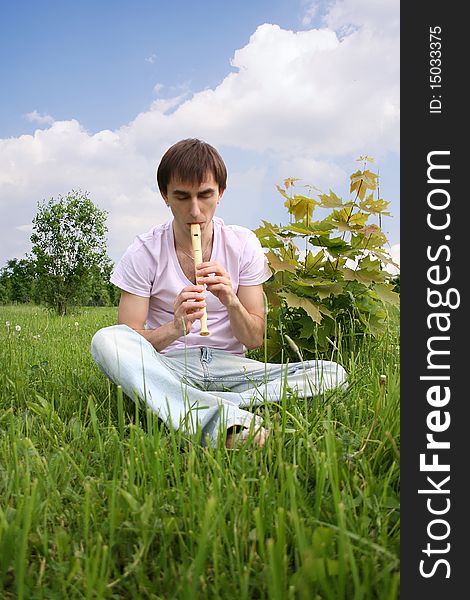 Young man playing on flute at summer time outdoor