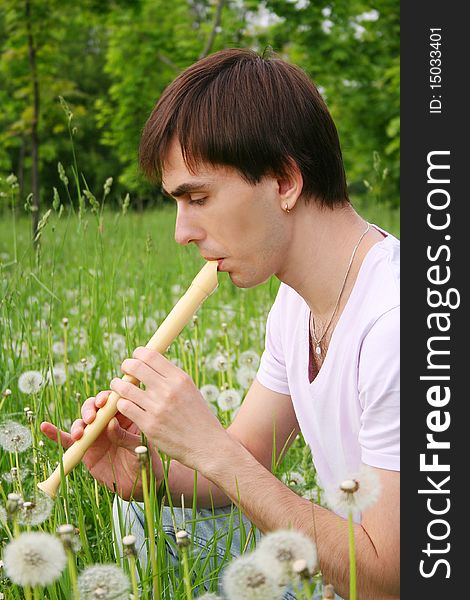 Young man playing on flute at summer time outdoor side view. Young man playing on flute at summer time outdoor side view