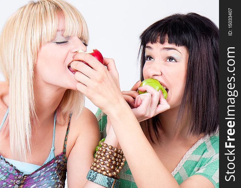 Two young pretty women bite a apples, studio shot