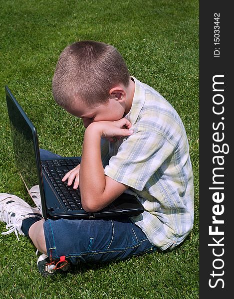 Boy playing with laptop outdoors on green grass