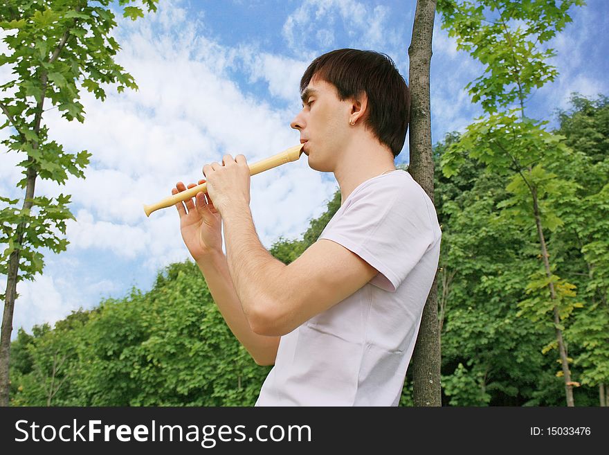 Young man playing on flute at summer time outdoor side view