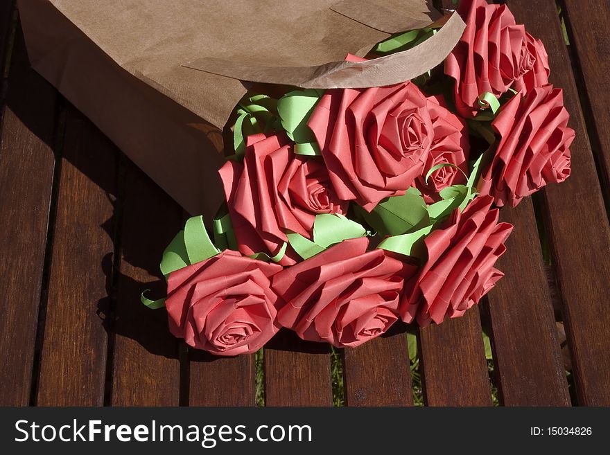 Red paper roses in a brown paper bag on a garden table