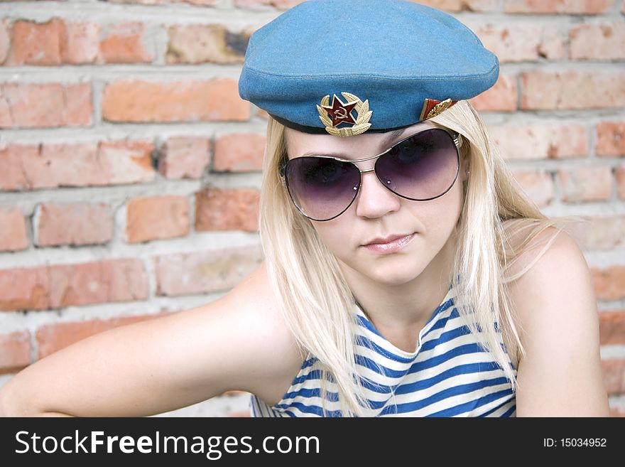 The woman in the military form and sun glasses sits near a brick wall. The woman in the military form and sun glasses sits near a brick wall