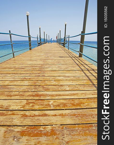 A small wooden jetty going into the sea from a tropical beach. A small wooden jetty going into the sea from a tropical beach