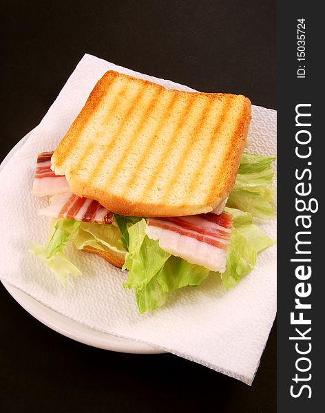 The toast with bacon, cheese and salad is prepared on a black background