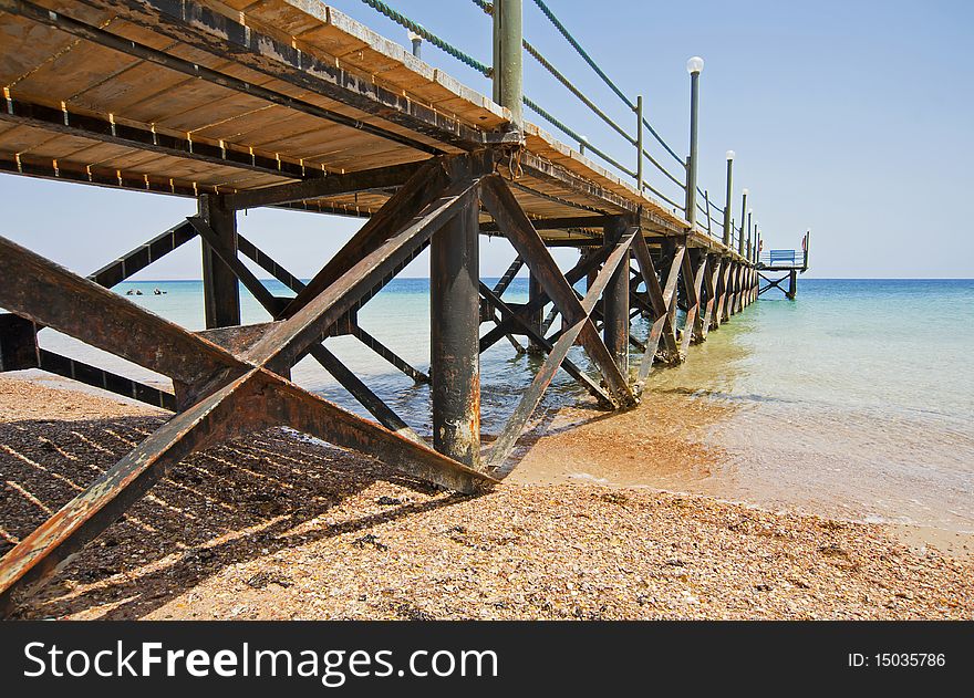 A small wooden jetty going into the sea from a tropical beach. A small wooden jetty going into the sea from a tropical beach