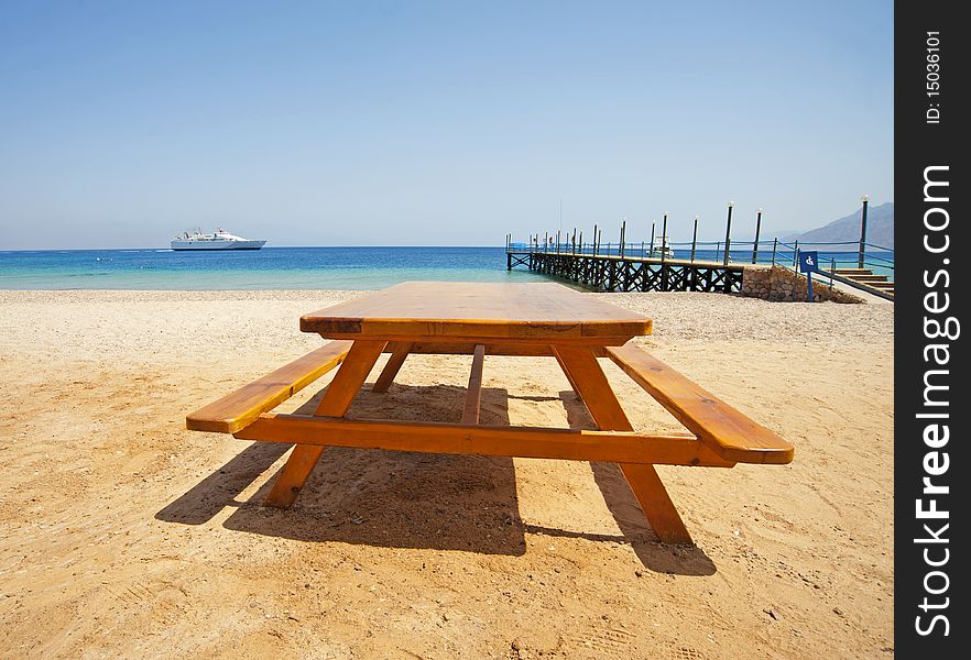 View from a tropical beach with a picnic table in the foreground and ferry at sea. View from a tropical beach with a picnic table in the foreground and ferry at sea