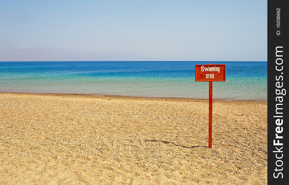 View out to sea from a tropical beach with a swimming area sign. View out to sea from a tropical beach with a swimming area sign