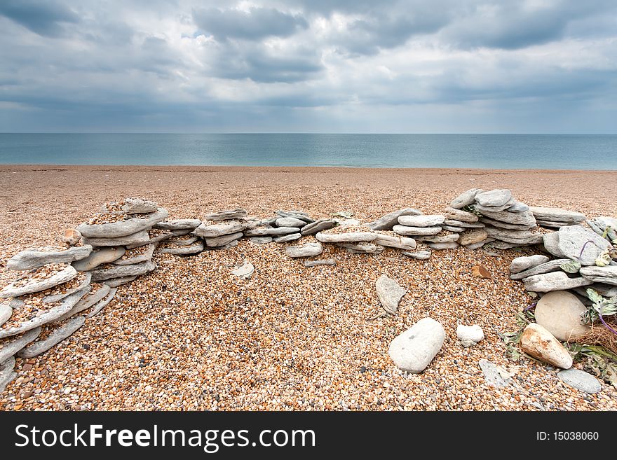 The remains of a stone wall on an empty shingle beach in Dorset, UK (Chesil Beach). The remains of a stone wall on an empty shingle beach in Dorset, UK (Chesil Beach)