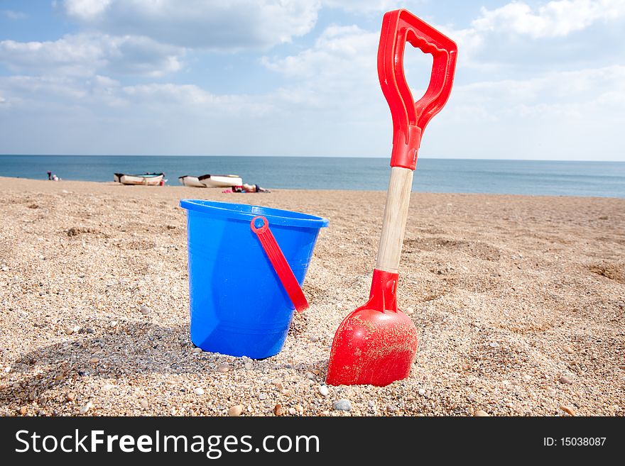 A blue bucket and a red spade on a sandy beach on a sunny afternoon. A blue bucket and a red spade on a sandy beach on a sunny afternoon.