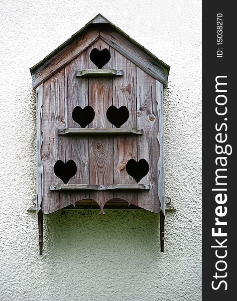 A vertical image of an ornate birdbox with heart shaped openings on a white wall. A vertical image of an ornate birdbox with heart shaped openings on a white wall