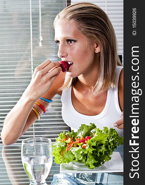 Young women at home biting on a strawberry eating a salad. Young women at home biting on a strawberry eating a salad