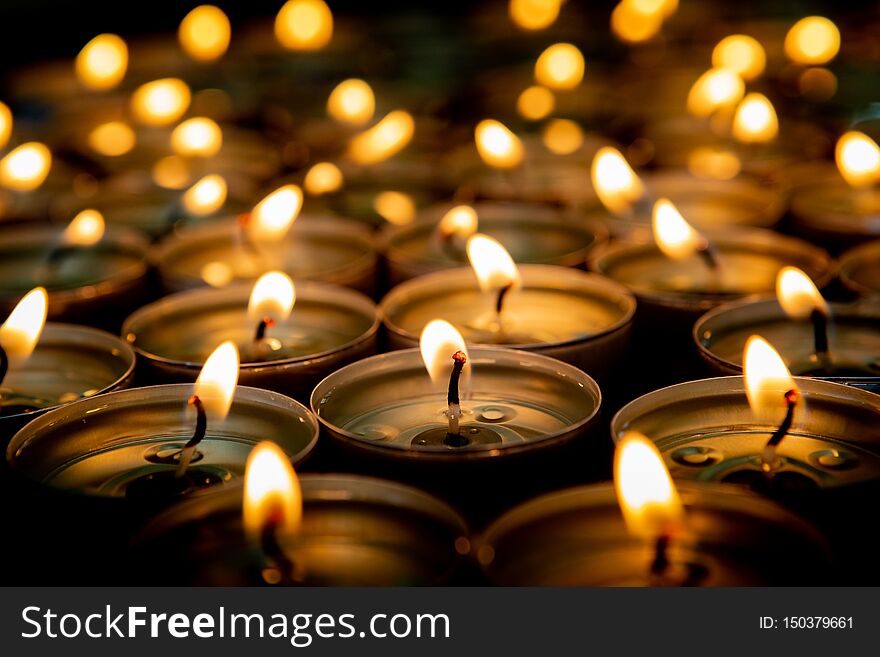 Many small burning candles on a wooden surface