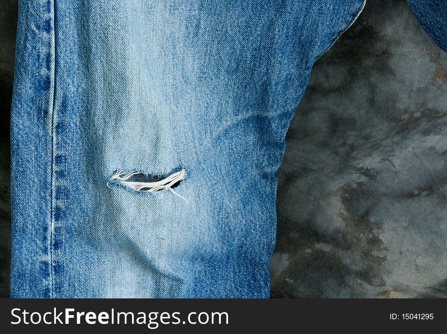 An old pair of blue jeans with a worn out knee showing the frayed threads. An old pair of blue jeans with a worn out knee showing the frayed threads.