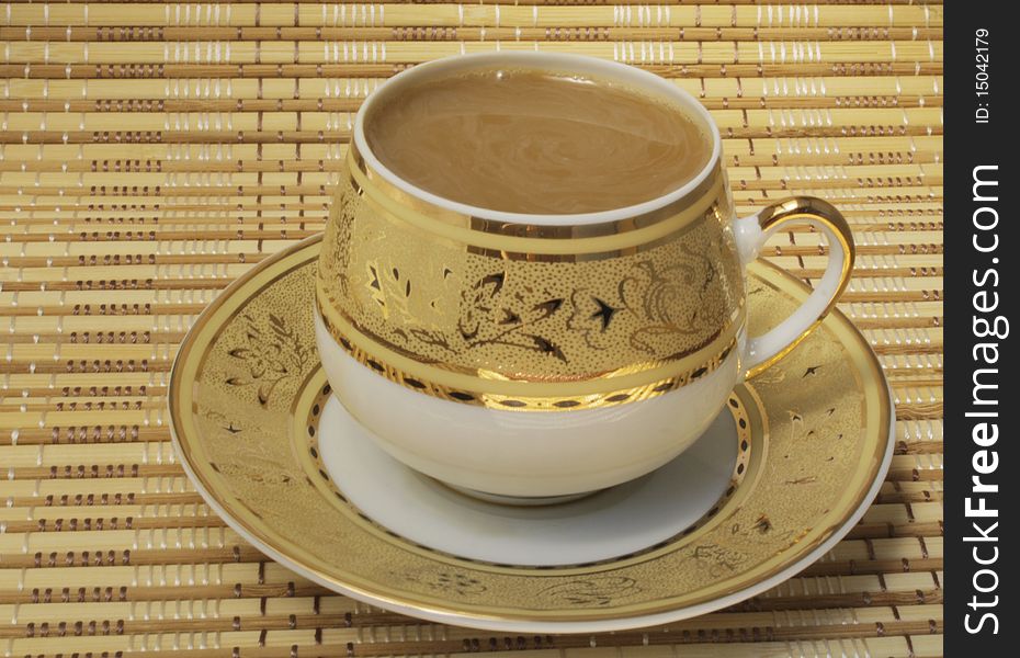 Coffee with milk in a cup with a gold pattern, cup and saucer on a bamboo cloth, the color of ocher