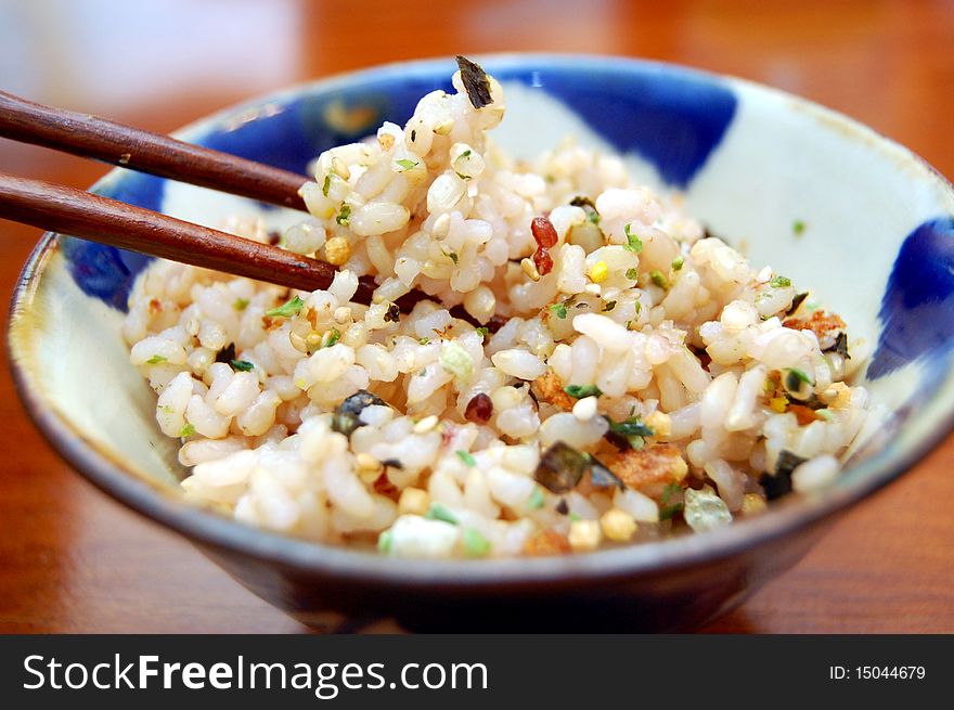 A rice bowl with seasoning and chopsticks holding up rice.