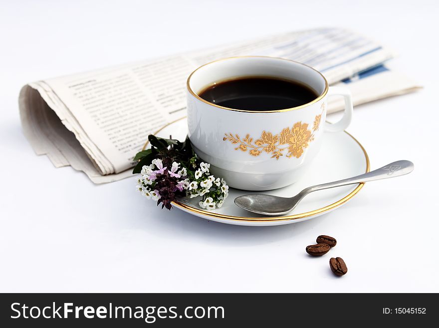 Cup with coffee on saucer, flowerses and newspaper