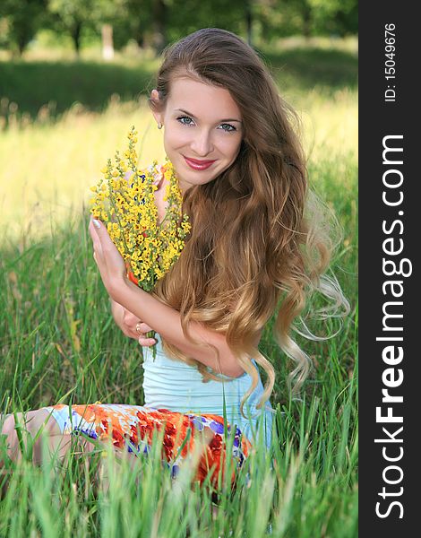 Young white girl in a green dress with long hair and pressed her hands with flowers to her chest look and smiling in green park. Young white girl in a green dress with long hair and pressed her hands with flowers to her chest look and smiling in green park