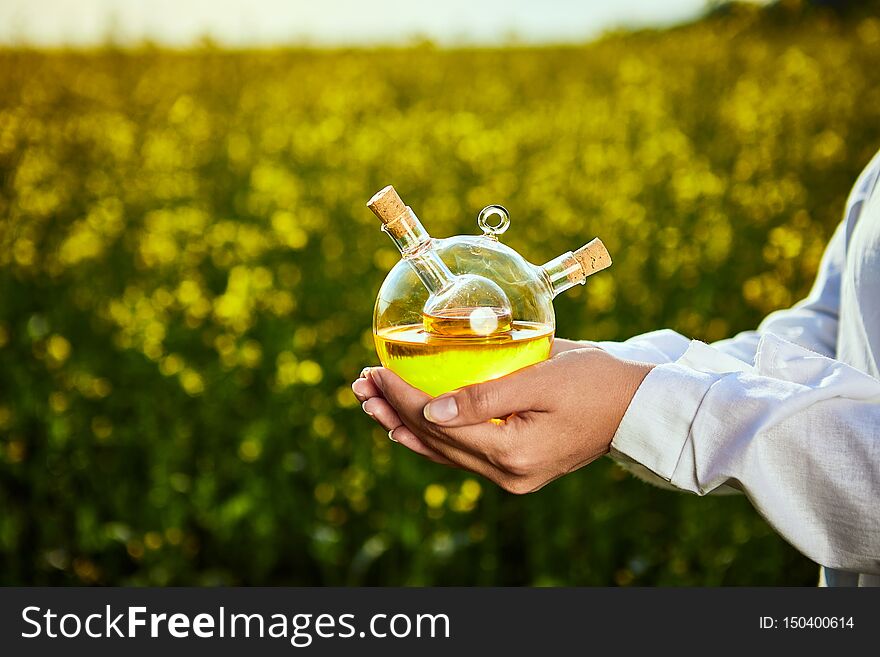 Rapeseed oil bottle in hand of an agronomist or biologist on background rape field