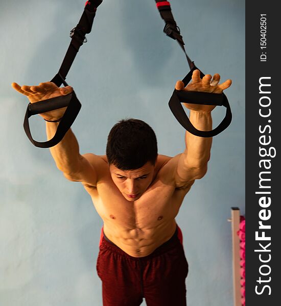 Young Man Does Workout In The Gym. Use TRX Or `Suspension Training`