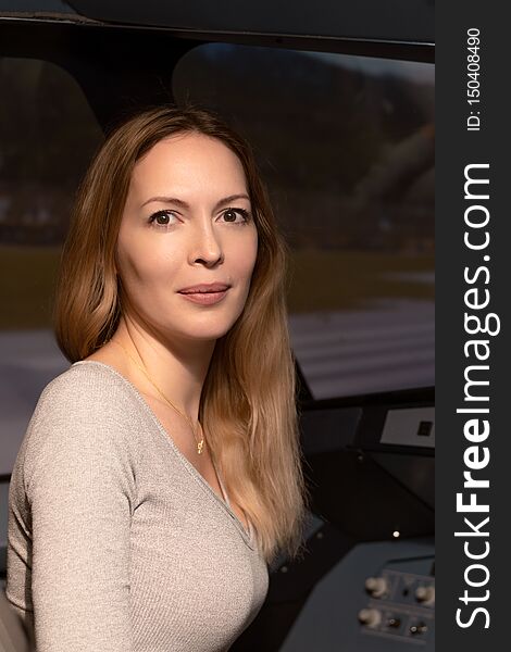 A young beautiful woman sits on the pilot`s seat in the seat at the helm and dashboard of an simulator airliner aircraft