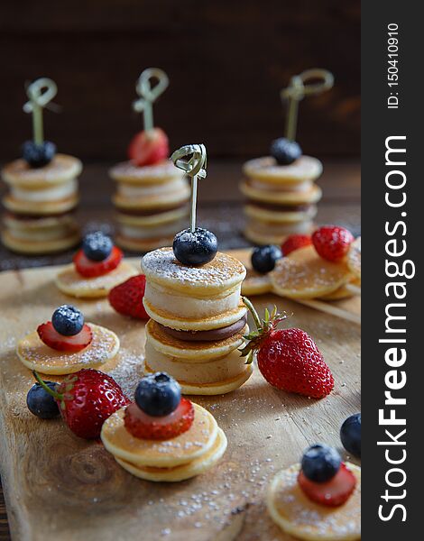 Fruit, berry and pancake canapes on wooden table