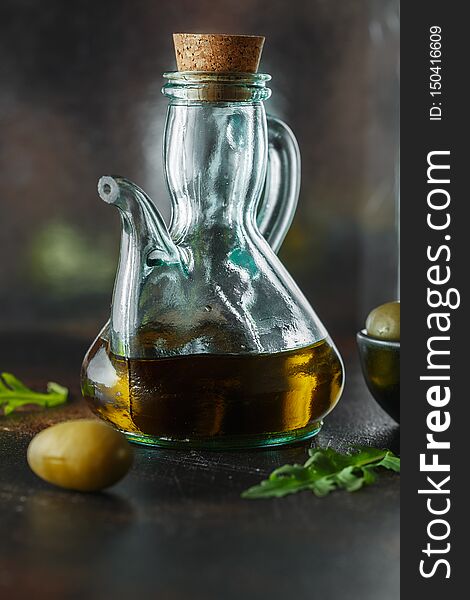 Fresh Organic Olive Oil in the jug on dark background. Food photography. Bottle of tasty olive oil. Glass jug of oil and canned olives