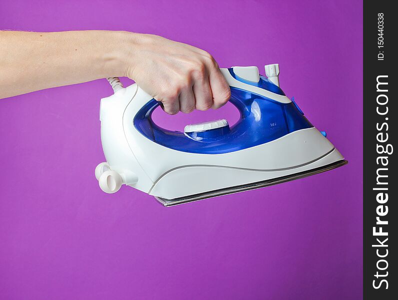 Female hand holding iron for ironing against purple background