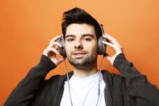 Free Happy Young Stylish Man Adjusting His Headphones And Smiling While Standing Against Orange Background Stock Image - 150451331