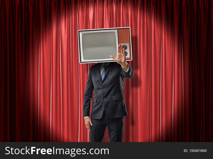 Businessman with vintage tv set instead of head making stop gesture on red stage curtains background