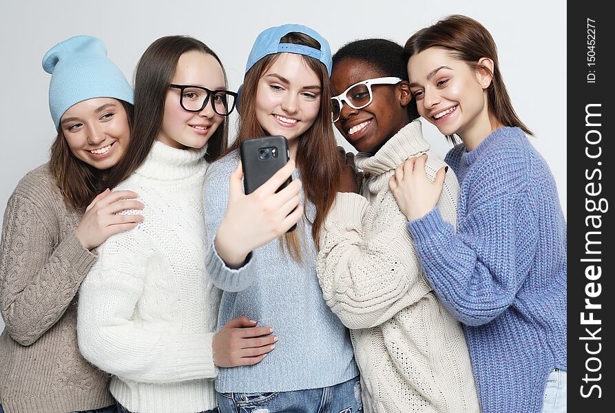 Lifestyle, friendship, tehnology and people concept: five different nation girls dressed in casual wear make selfie with a smartphone over white background