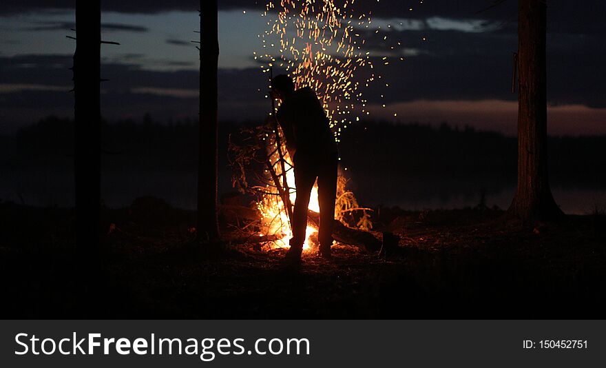 Silhouette of a man near the fire at night against the sky.