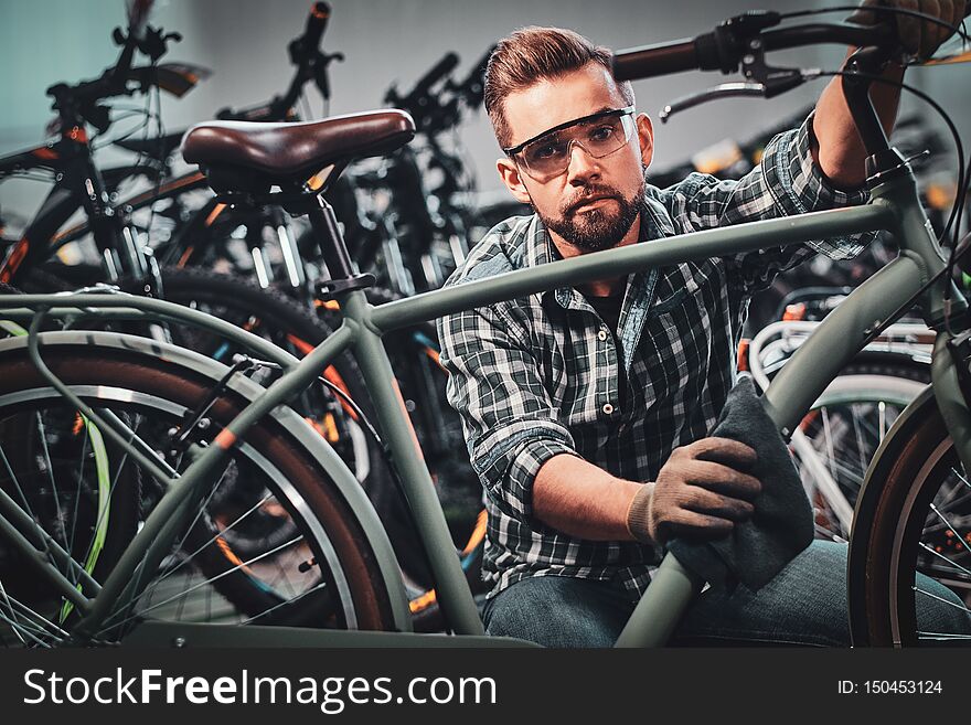 Busy attractive man in protective glasses is cleaning one of bicycle from dust.