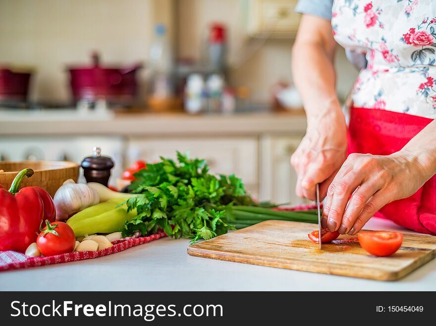 Female Hand With Knife Chops Tomato In Kitchen. Cooking Vegetables