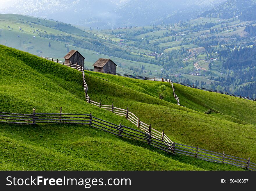 Landscape of a raw green meadow with leading lines to barns, Bucovina, Romania.
