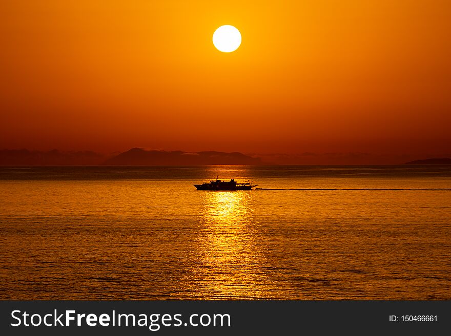 Silhouette of a ship passing in the reflection of the Sun in the Ionian Sea, Sarande, Albania. Ship passing by sun reflection, with Corfu island in the background.