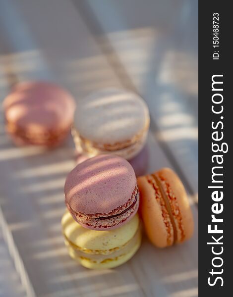 Sweet French pastries on a rustic table. Dessert macarons in the summer evening in the orchard. Natural blurred background.