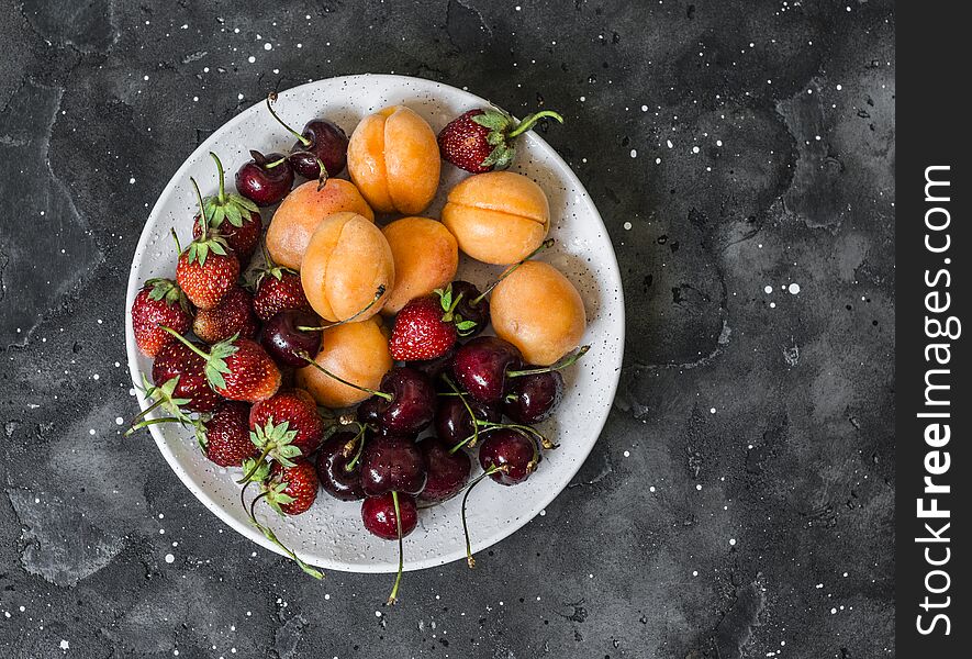 Fresh ripe fruit - apricots, cherries, strawberries on a dark background, top view