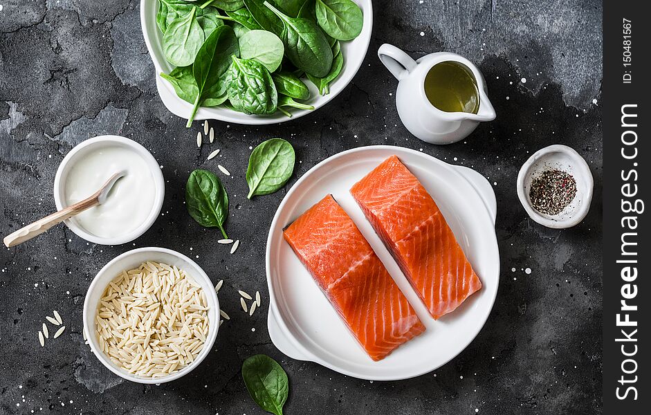 Ingredients for a balanced lunch - salmon fish, spinach, cream, orzo pasta on a dark background, top view