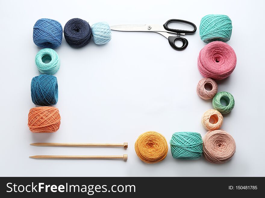 Frame made with clews of colorful knitting threads and accessories on white background, flat lay